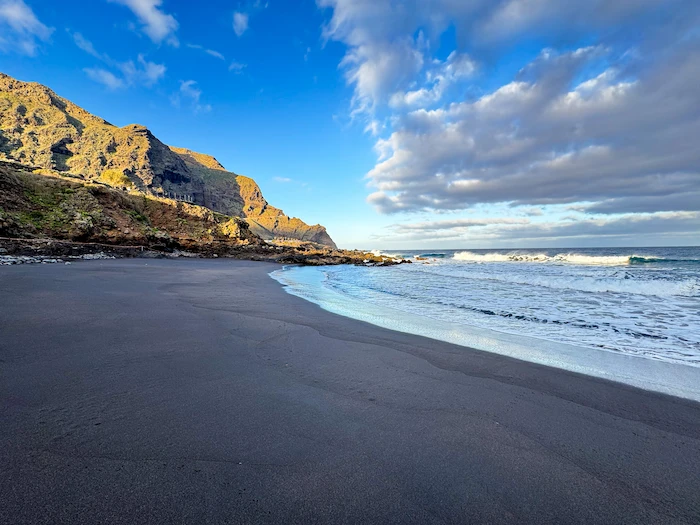 Wide black sand beach in Tenerife with waves and cliffs
