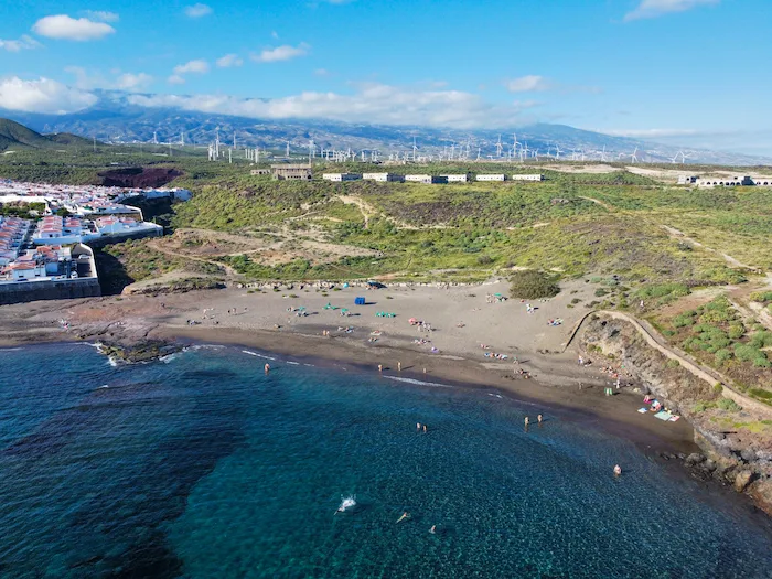 Abades Beach Tenerife with swimmers and small waves, view of the town in the distance.