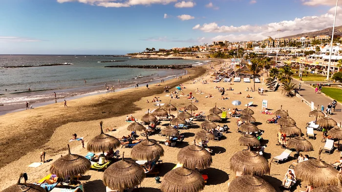 Playa Fañabé beach with straw umbrellas, sunbeds, and families relaxing