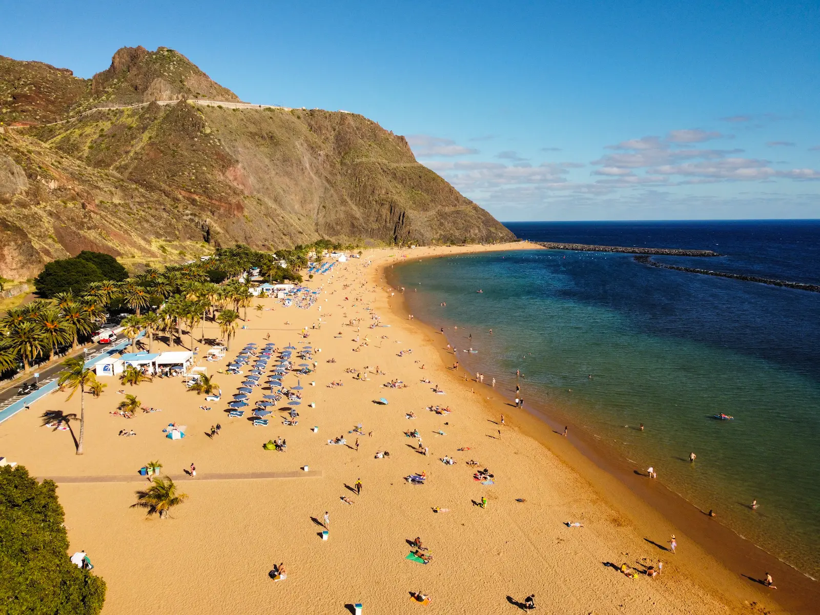Aerial view of Playa de Las Teresitas with golden sand, umbrellas, and cliffs in the background.