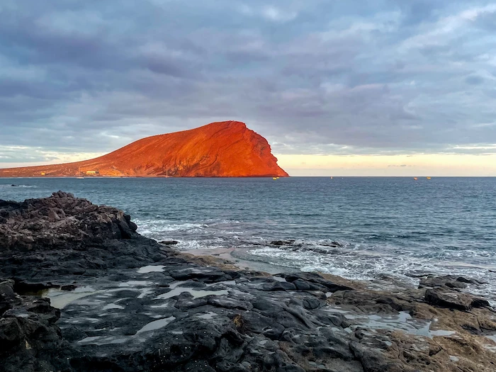 Montaña Roja glowing red at sunset, seen from the rocky coastline