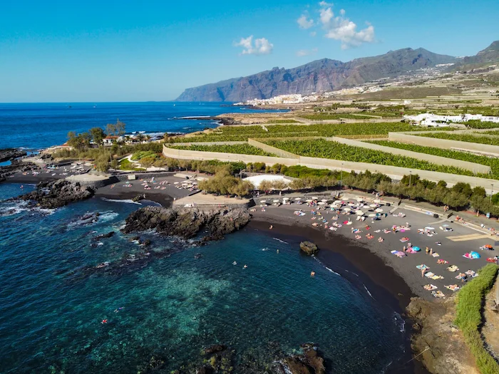 Playa de Alcalá in Tenerife seen from above, with black sand, clear ocean water, and green farmland