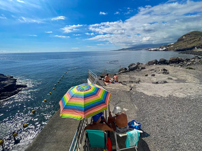 Woman sitting by the sea with rainbow umbrella, Tenerife