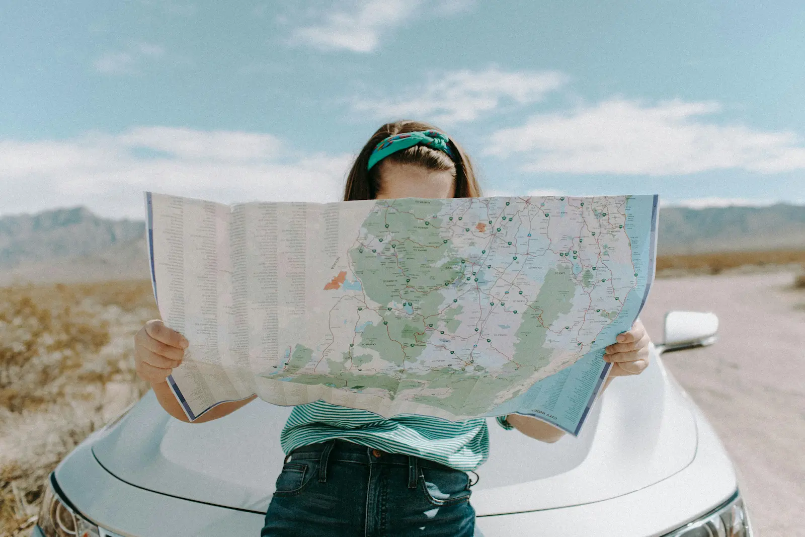 Woman holding a large map while planning a road trip next to her car