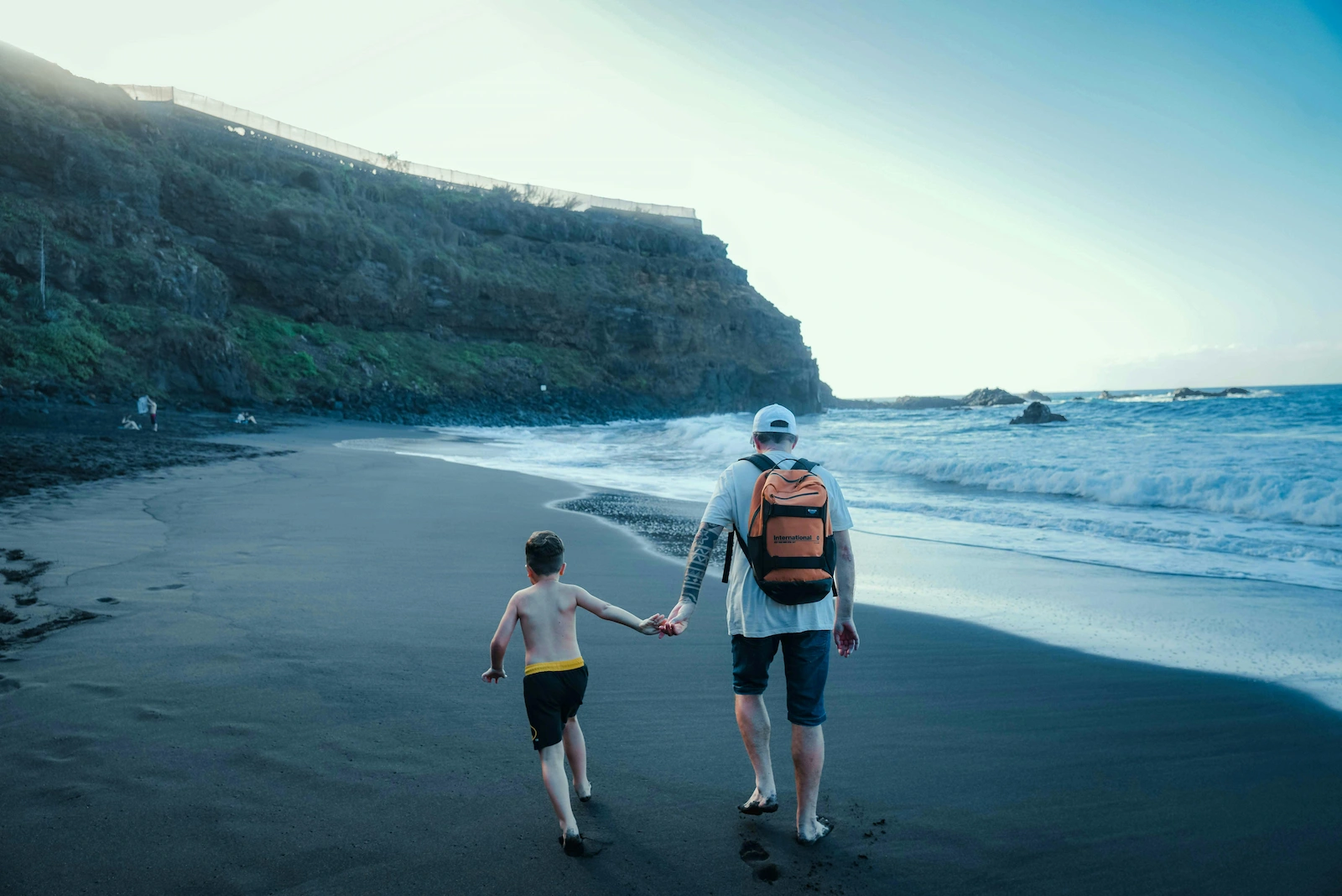 Parent and child walking on a black sand beach in Tenerife